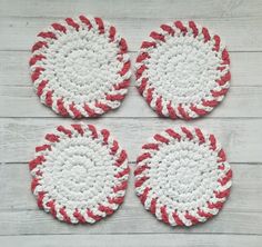 four red and white crocheted coasters sitting on top of a wooden table