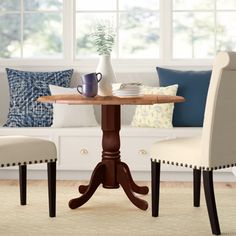 a table with two chairs and a vase on it in front of a window filled with pillows