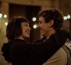 a man and woman hugging each other in the middle of a room with lights on