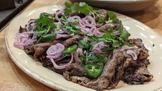 a white plate topped with meat and onions on top of a wooden table next to a bowl