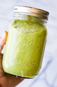 a hand holding a mason jar filled with green smoothie