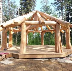 a wooden gazebo sitting on top of a dirt ground next to trees in the woods