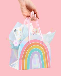 a hand is holding a bag with a rainbow design on it, against a pink background