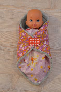 a doll in a pink and orange blanket on a wooden floor next to a white wall