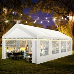 a large white tent with people sitting at tables under string lights on the grass in front of it