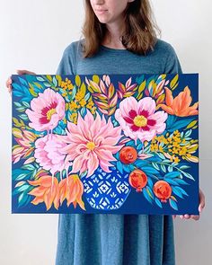 a woman holding up a large painting with flowers on it's back and blue background