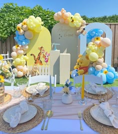 a winnie the pooh birthday party set up with balloons, plates and napkins