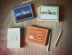 three matchboxes sitting on top of a wooden table next to matchesticks