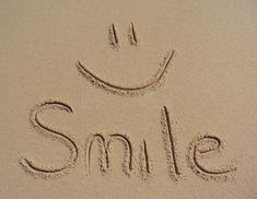 the word smile written in sand with a smiley face drawn on it's side