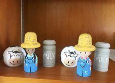 some little toy figures are sitting on a wooden shelf next to two jars and one is wearing a fireman's hat