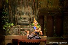 a woman sitting on top of a wooden bench next to a large statue in the background