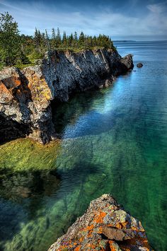 the water is crystal green and clear with rocks on both sides, and trees in the background