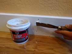 a person holding a paintbrush next to a bucket of white paint on a wooden floor