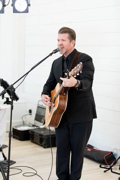 a man in a suit singing into a microphone and playing an acoustic guitar on stage