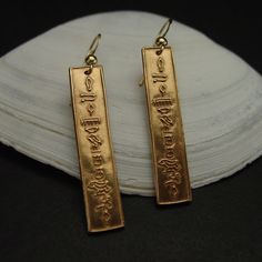 "Hand carved charm in hieroglyphics stating discreetly \"Eternal Love\" which makes perfect Egyptian cartouche earrings. As for \"Eternal Life\" represented in the Ankh here we have \"Eternal Love\" as it truly never dies. This is a more modern dainty and feminine version of the traditional cartouche designs. - Hand carved charms - Solid yellow bronze also called jeweler gold bronze charms. - The charms are about 1.25\" long. - 14k gold filled ear wire - Gold filled has 100 times more gold than Engraved Brass Earrings For Anniversary, Bronze Spiritual Earrings As Gift, Spiritual Bronze Earrings Gift, Symbolic Engraved Gold Earrings, Gold Engraved Symbolic Earrings, Engraved Gold Symbolic Earrings, Ancient Egypt Hieroglyphics, Egypt Hieroglyphics, Egyptian Jewelry