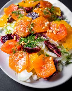 a white plate topped with oranges and fennel on top of a black table