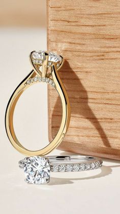 an engagement ring and wedding band sitting next to each other on a white surface with a wooden box in the background