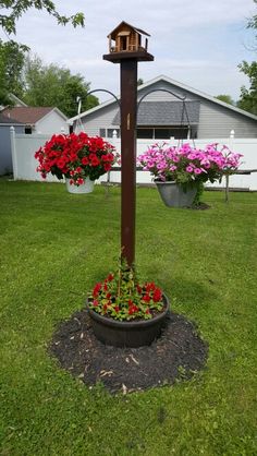 a birdhouse on top of a pole with flowers around it