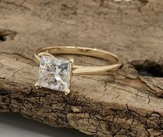 a gold ring with a princess cut diamond in the center on a piece of wood