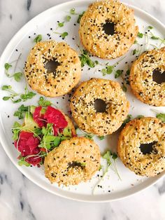 four bagels with sesame seeds and sprinkles on a white plate