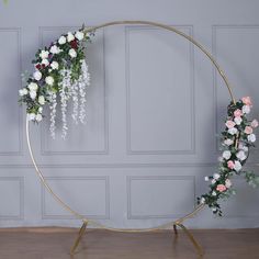 a circular gold frame with flowers and greenery hanging from the side on a wooden floor