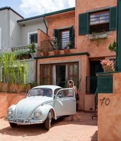 a white car parked in front of a pink building with green shutters and windows