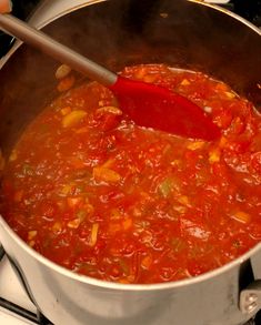 a pot on the stove with a red spoon in it, full of chili sauce