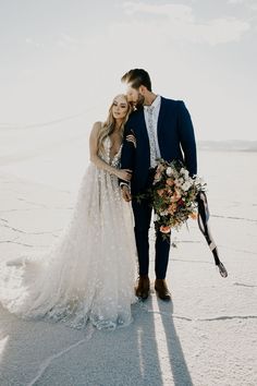 a bride and groom standing in the snow with their arms around each other holding bouquets