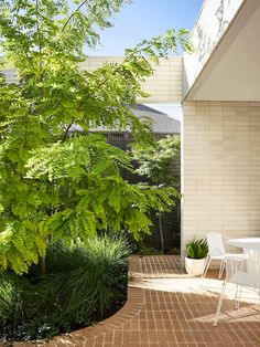 a white table and chairs sitting on top of a brick floor next to a tree