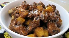 a bowl filled with meat and potatoes on top of a flowered table cloth next to a spoon