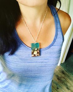 a woman wearing a blue shirt with a green and white pendant on it's neck