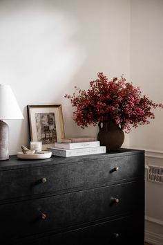 a vase with red flowers sitting on top of a black dresser next to a lamp