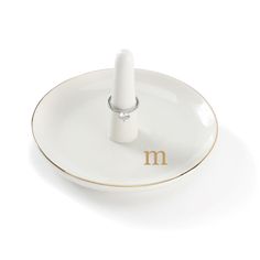 a small white candle holder with the letter m on it's side, sitting on a plate