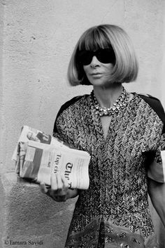 a woman in sunglasses is holding a newspaper