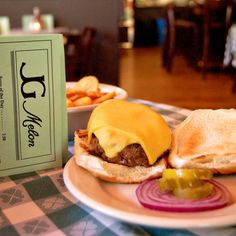 a hamburger with cheese and pickles on a plate next to a box of chips