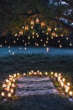 candles are arranged in the shape of a heart on a blanket under a large tree