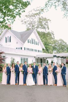 a large group of people standing in front of a white house with pink bouquets