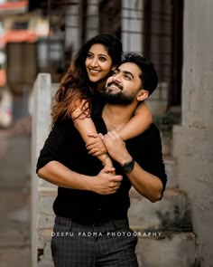 a man holding a woman in his arms while she smiles at the camera with her arm around him