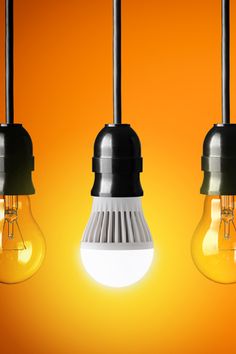 three light bulbs hanging from the ceiling in front of an orange background with one bulb turned on