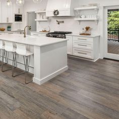 a large kitchen with white cabinets and counter tops, along with bar stools that match the hardwood flooring