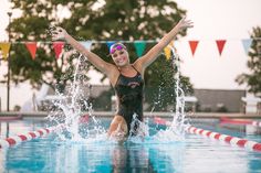 a woman in a swimming suit is jumping into the pool with her arms spread out