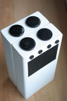 a white box with black buttons on the front and sides, sitting on a wooden surface