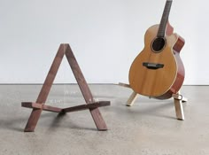 an acoustic guitar sitting on top of a wooden stand next to another instrument that is leaning against the wall