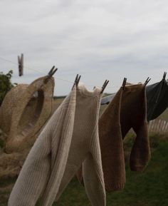 three pairs of socks hanging from clothesline with grass in the back ground and clouds in the background