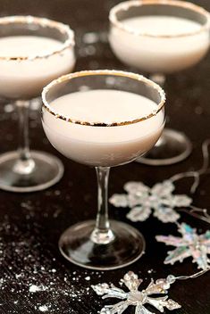 three glasses filled with white liquid on top of a black table covered in snowflakes