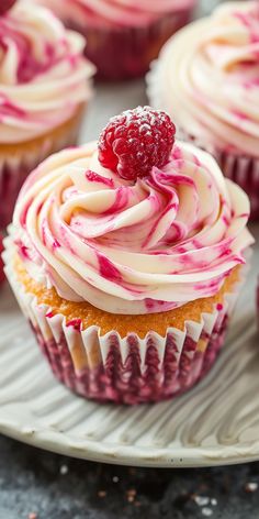 cupcakes with white frosting and raspberry toppings on a plate