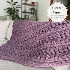 a purple crochet blanket sitting on top of a couch next to a white pillow