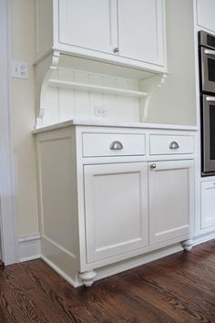 an empty kitchen with white cabinets and wood floors