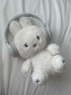 a white teddy bear laying on top of a bed with headphones