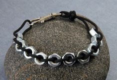 a close up of a bracelet on a rock with a black cord and silver links